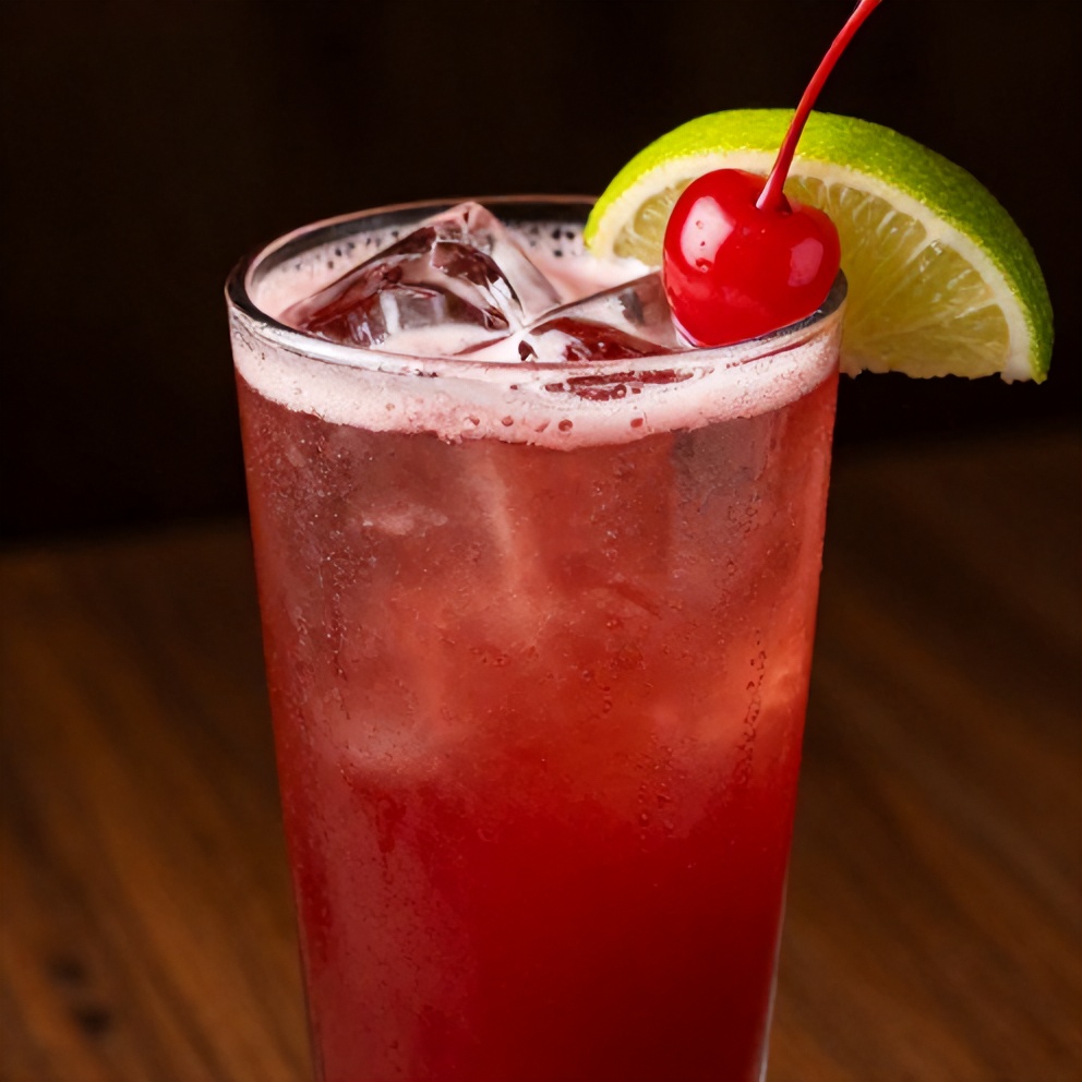 A glass of Cherry Limeade with a lime wedge and cherry garnish